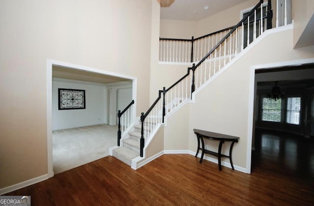 staircase with hardwood / wood-style floors, a towering ceiling, and a notable chandelier