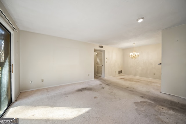 spare room featuring light colored carpet and a chandelier