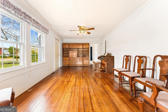 living area with built in shelves, hardwood / wood-style floors, ceiling fan, and ornamental molding