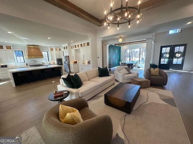 living room featuring french doors, a chandelier, ornamental molding, light wood-type flooring, and decorative columns