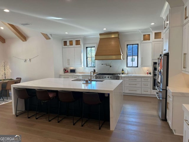 kitchen featuring white cabinets, premium range hood, a kitchen island with sink, and hardwood / wood-style floors