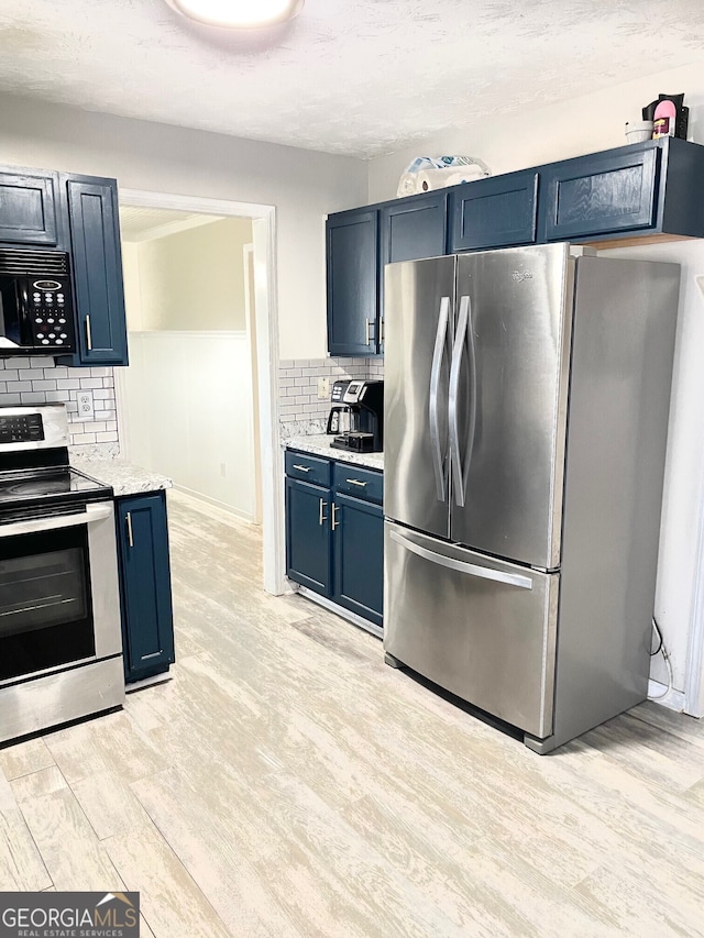 kitchen with blue cabinetry, tasteful backsplash, light stone counters, appliances with stainless steel finishes, and light wood-type flooring