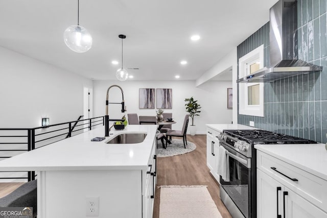 kitchen featuring stainless steel stove, a center island with sink, white cabinetry, and wall chimney exhaust hood