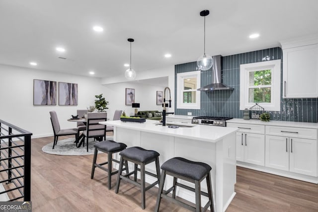 kitchen with sink, wall chimney range hood, a center island with sink, range, and white cabinetry