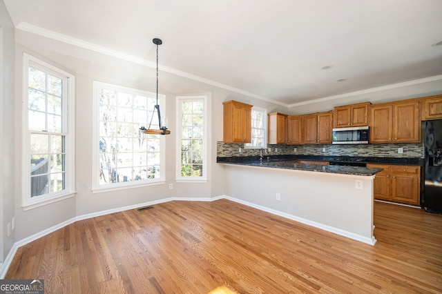 kitchen with backsplash, black fridge, decorative light fixtures, light hardwood / wood-style floors, and kitchen peninsula