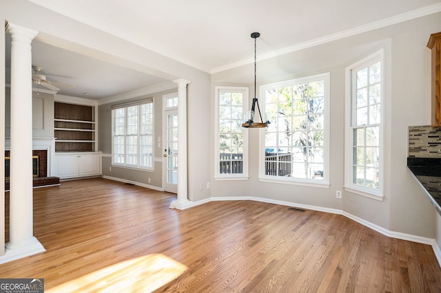 unfurnished dining area with a brick fireplace, plenty of natural light, ceiling fan with notable chandelier, and hardwood / wood-style flooring