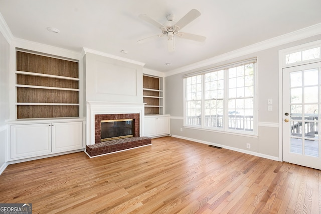 unfurnished living room featuring a brick fireplace, built in features, ornamental molding, and light hardwood / wood-style flooring