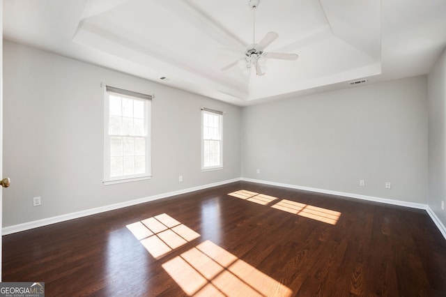 unfurnished room with a tray ceiling, ceiling fan, and dark wood-type flooring