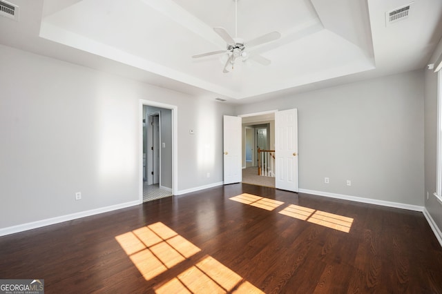 unfurnished room featuring a raised ceiling, ceiling fan, and dark wood-type flooring