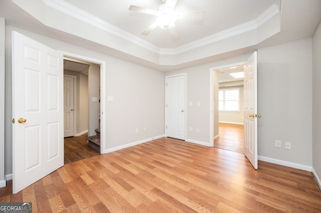 unfurnished bedroom with a tray ceiling, crown molding, hardwood / wood-style floors, and ceiling fan