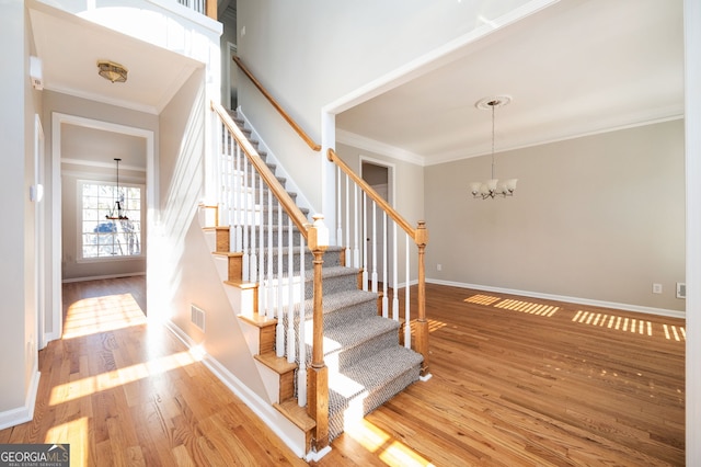 stairs featuring hardwood / wood-style flooring, a notable chandelier, and ornamental molding