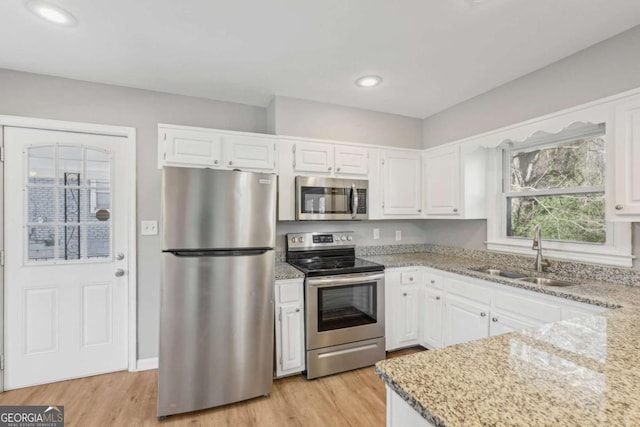 kitchen with appliances with stainless steel finishes, a sink, light wood-style flooring, and light stone countertops