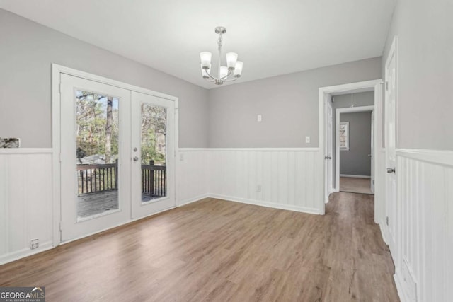 unfurnished dining area featuring light wood-type flooring, french doors, wainscoting, and a notable chandelier