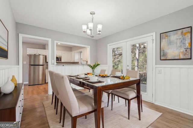 dining room with light wood finished floors, a notable chandelier, and a wainscoted wall