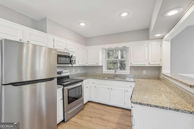 kitchen featuring light stone counters, appliances with stainless steel finishes, white cabinets, and a sink