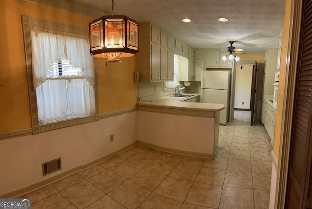 kitchen with white appliances, a peninsula, visible vents, ceiling fan with notable chandelier, and a sink
