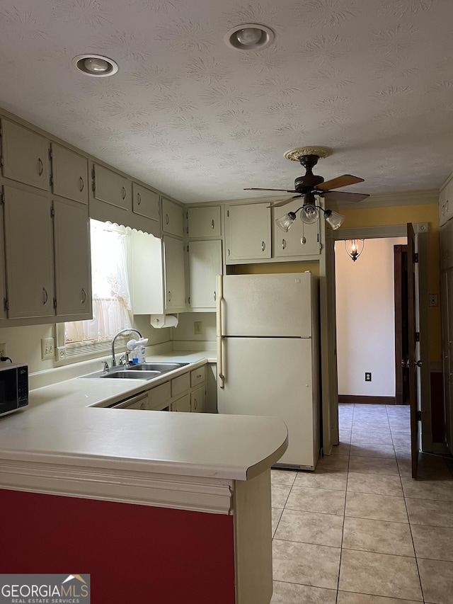 kitchen with light countertops, freestanding refrigerator, a sink, black microwave, and a peninsula