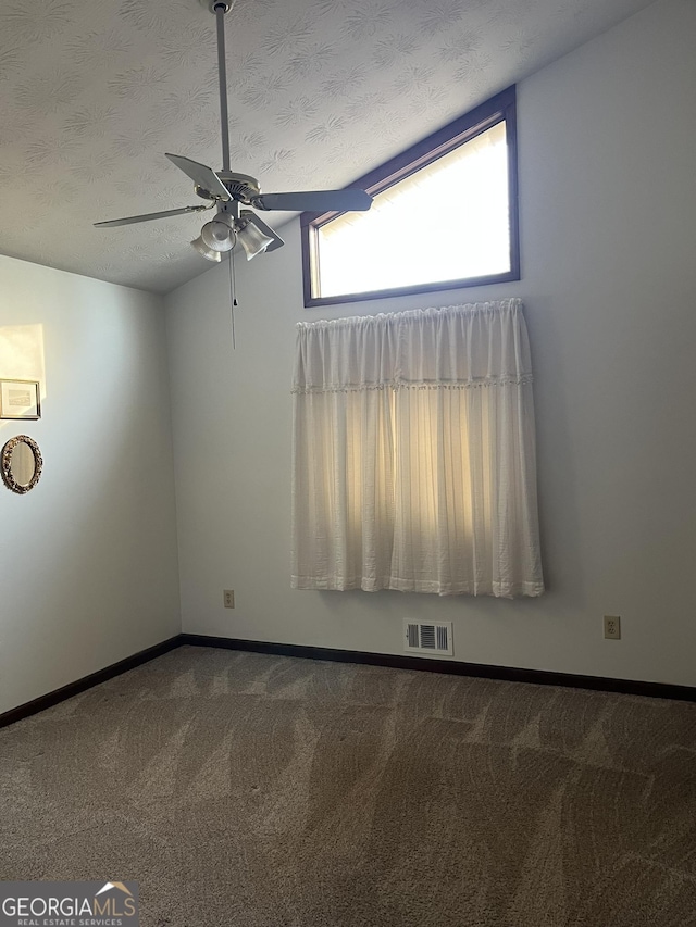 carpeted empty room with baseboards, visible vents, a ceiling fan, vaulted ceiling, and a textured ceiling