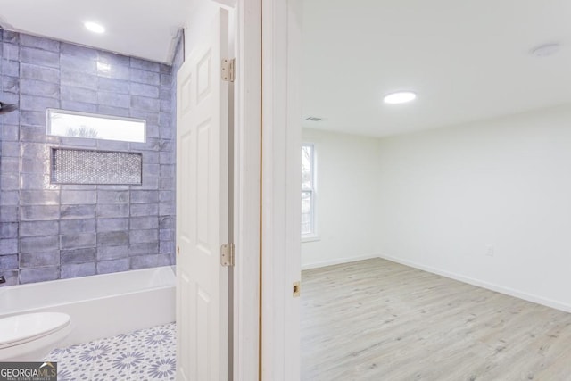 bathroom featuring hardwood / wood-style flooring, tiled shower / bath combo, a healthy amount of sunlight, and toilet