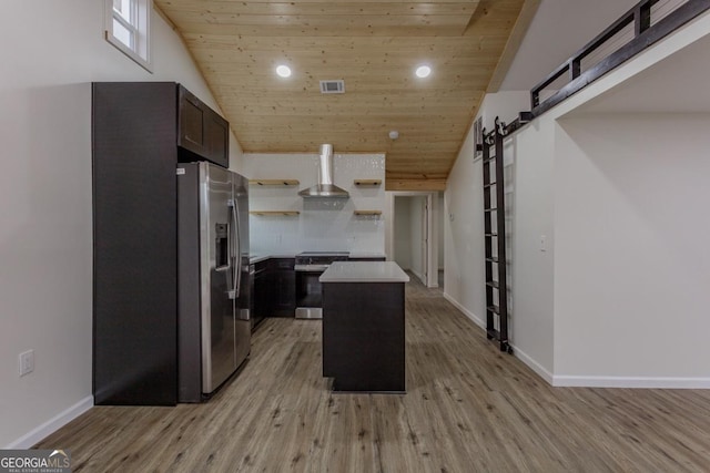 kitchen with light wood-type flooring, wall chimney exhaust hood, stainless steel appliances, a barn door, and a center island