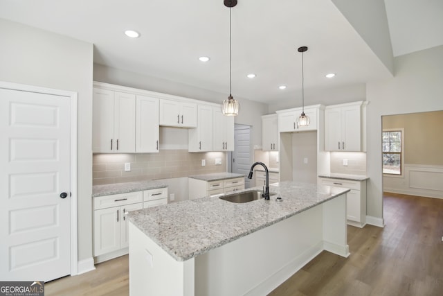 kitchen featuring white cabinets, a center island with sink, light stone countertops, and sink