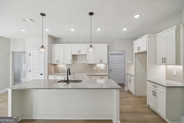 kitchen with white cabinets, hanging light fixtures, a kitchen island with sink, and sink