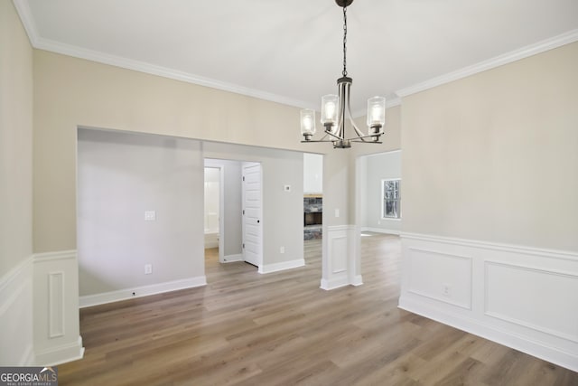 unfurnished dining area with wood-type flooring, ornamental molding, and an inviting chandelier