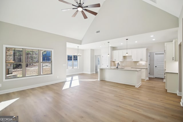 unfurnished living room featuring ceiling fan with notable chandelier, a wealth of natural light, sink, and high vaulted ceiling