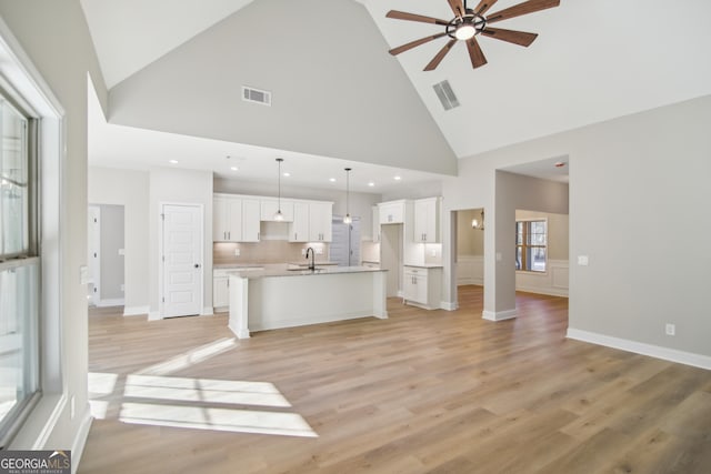 kitchen with sink, high vaulted ceiling, decorative light fixtures, a center island with sink, and white cabinets