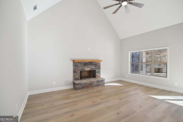 unfurnished living room with a stone fireplace, ceiling fan, high vaulted ceiling, and light wood-type flooring