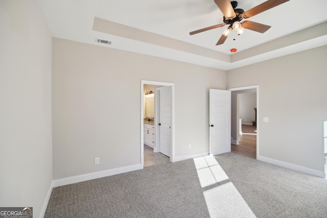 unfurnished bedroom featuring light carpet, connected bathroom, a raised ceiling, and ceiling fan