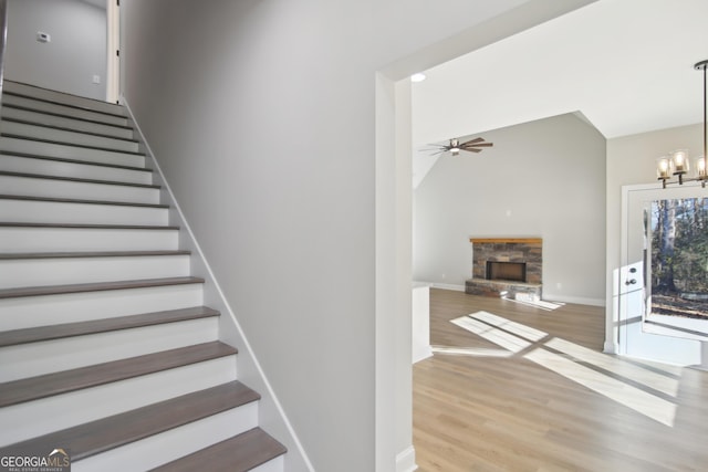 stairs with lofted ceiling, a fireplace, hardwood / wood-style floors, and ceiling fan with notable chandelier