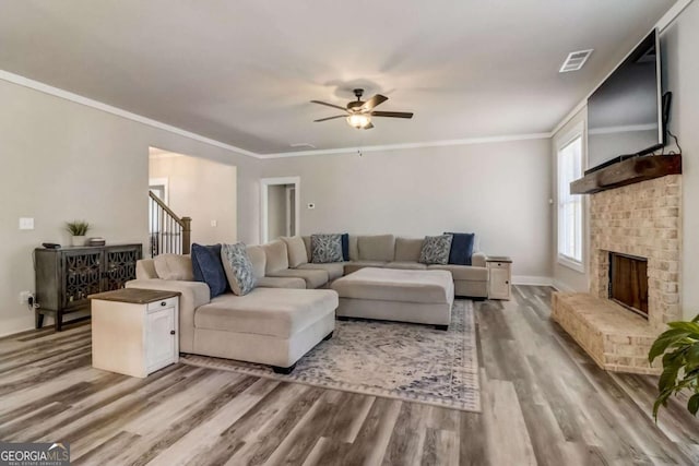 living room featuring hardwood / wood-style floors, ceiling fan, crown molding, and a brick fireplace