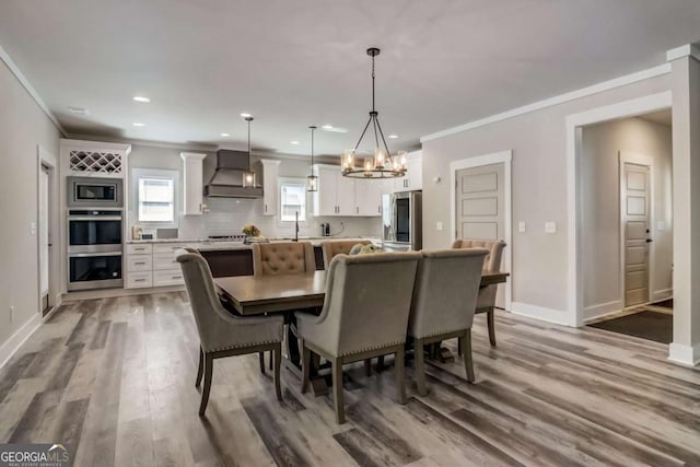 dining area with sink, wood-type flooring, ornamental molding, and a chandelier