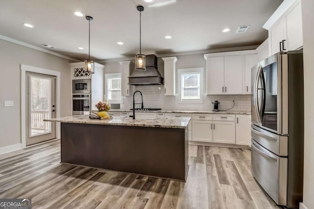 kitchen featuring a center island with sink, decorative light fixtures, custom range hood, and stainless steel appliances