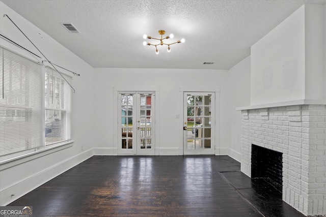 unfurnished living room with a brick fireplace, dark wood-type flooring, a notable chandelier, and a textured ceiling