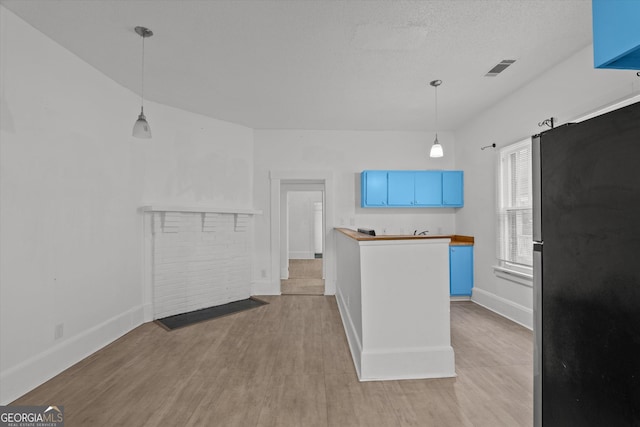 kitchen with blue cabinetry, wooden counters, decorative light fixtures, stainless steel fridge, and light hardwood / wood-style floors