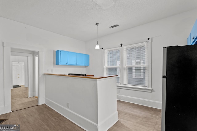 kitchen with blue cabinetry, stainless steel refrigerator, wood-type flooring, a textured ceiling, and decorative light fixtures