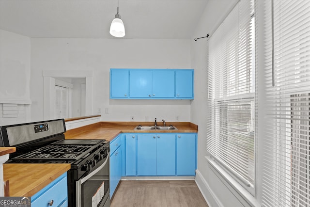 kitchen with blue cabinetry, sink, gas stove, wooden counters, and hanging light fixtures