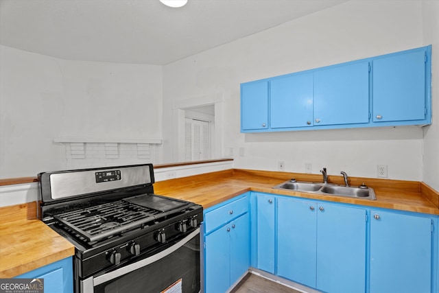 kitchen with butcher block countertops, stainless steel range with gas cooktop, blue cabinetry, and sink