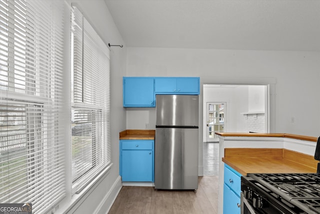 kitchen featuring black gas range oven, blue cabinetry, stainless steel refrigerator, and wooden counters