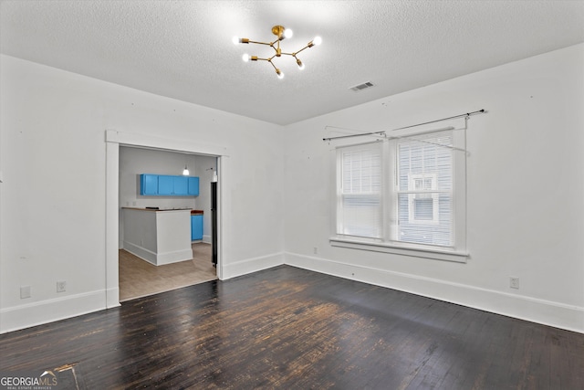 empty room with dark hardwood / wood-style flooring, a chandelier, and a textured ceiling