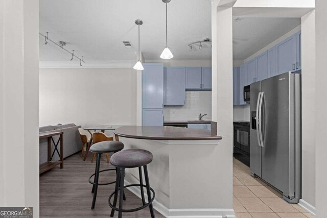 kitchen with a breakfast bar, blue cabinets, stainless steel fridge, tasteful backsplash, and decorative light fixtures