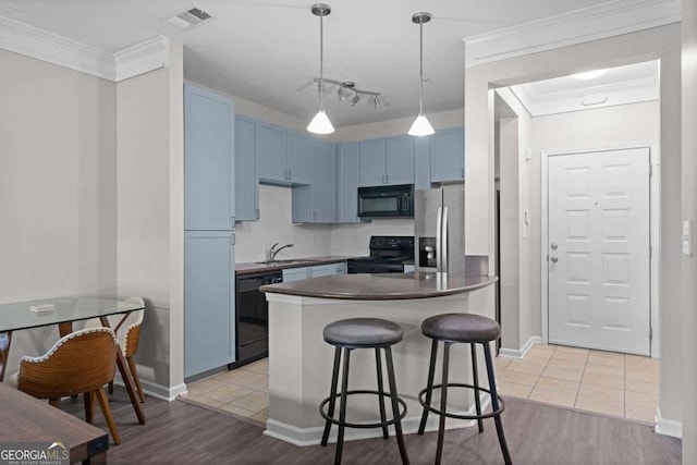 kitchen with sink, hanging light fixtures, light hardwood / wood-style floors, a breakfast bar area, and black appliances