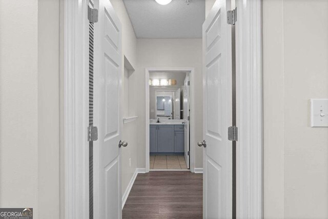 corridor with a textured ceiling, dark wood-type flooring, and sink