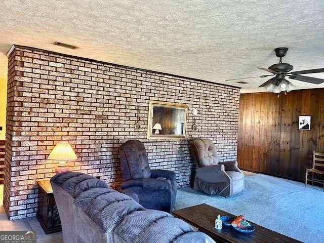 living room with a textured ceiling, ceiling fan, wood walls, and brick wall