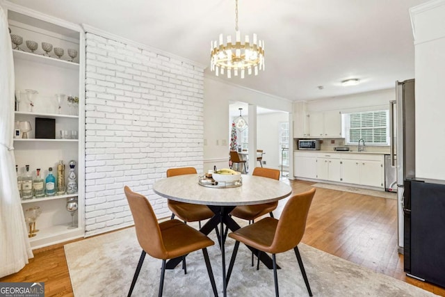 dining space featuring crown molding, light hardwood / wood-style floors, brick wall, and a notable chandelier