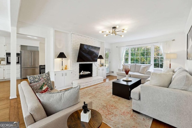 living room featuring hardwood / wood-style floors, an inviting chandelier, crown molding, and a brick fireplace