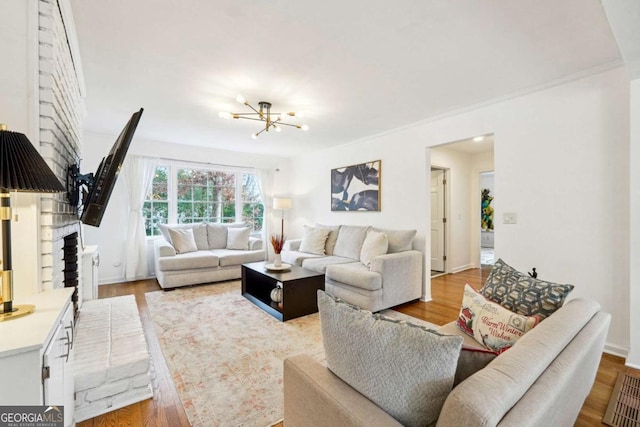 living room featuring wood-type flooring, a brick fireplace, a notable chandelier, and crown molding