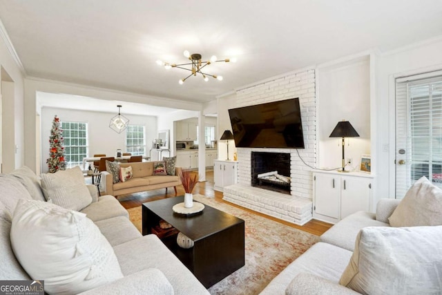 living room with a notable chandelier, light hardwood / wood-style floors, ornamental molding, and a brick fireplace